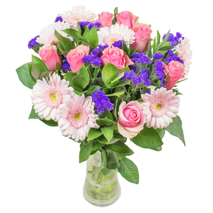 Centred against a pristine background, this vibrant floral arrangement brings together approximately 7-9 soft pink roses-each capturing the eye with either a classical spiral form or a hint of fresh, unfolding bloom. Intermixed are 5-7 pale pink gerbera daisies, whose wide, gently radiating petals frame the bouquet with a calm, optimistic light. Small clouds of striking purple statice weave between the larger blossoms, offering textured brilliance and a pop of colour much like the vivid flowerbeds near Orpington High Street. At the base, lush green foliage lends calming structure and fullness, setting off the gentle hues above. The stems settle gracefully within a transparent vase, where they are held by clear, revitalizing water-a testament to freshness and care found at Orpington Florist. Ideal for birthdays, anniversaries, or as a memorable gift for Mother's Day, this display fills any home or office with an air of celebration, serenity, and Orpington's distinctive local flair.
